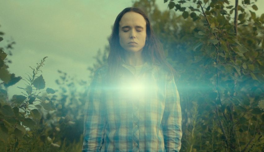 A woman standing in a field with a glowing light in her eyes.