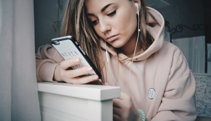 A girl in a pink hoodie with earphones looking at her phone.