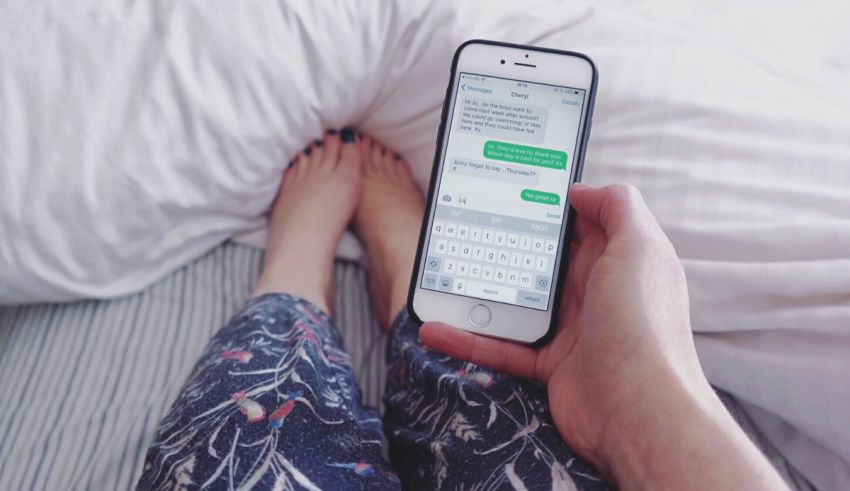 A woman's feet holding a cell phone in bed with a text message on it.