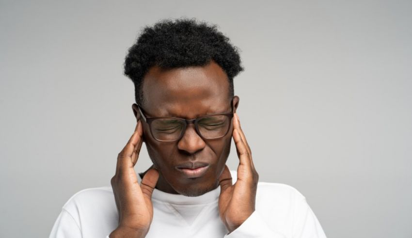 A black man with a headache holding his hands over his ears.
