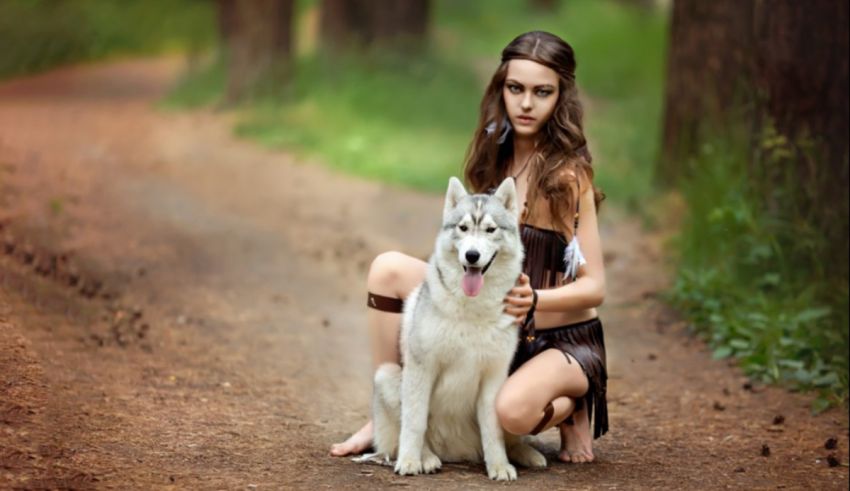 A woman with a white husky dog in the woods.