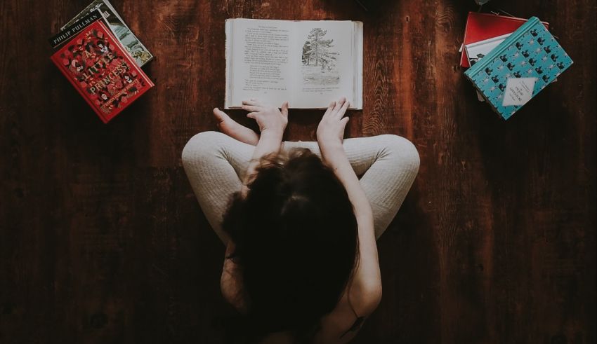 A woman reading a book on a wooden floor.