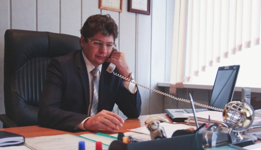 A man in a suit talking on the phone at his desk.