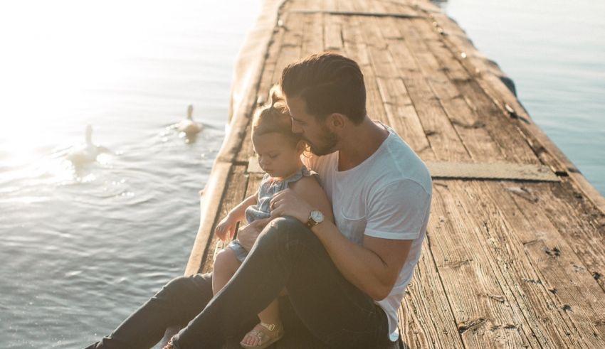 A man and his daughter sitting on a dock.