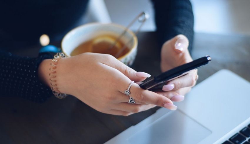 A woman's hand holding a cell phone next to a laptop.