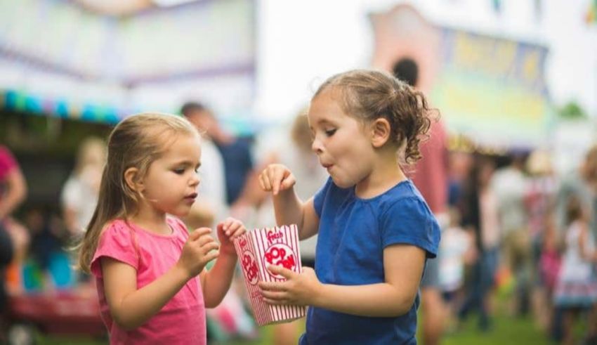 Two little girls eating popcorn at a fair.