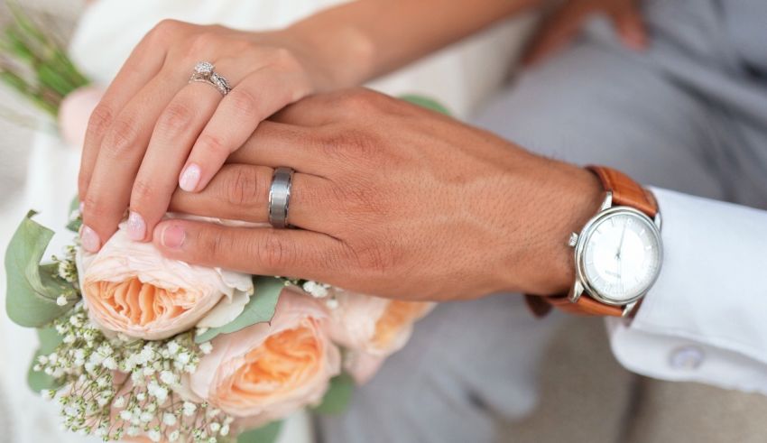 The hands of a bride and groom holding a bouquet of roses.