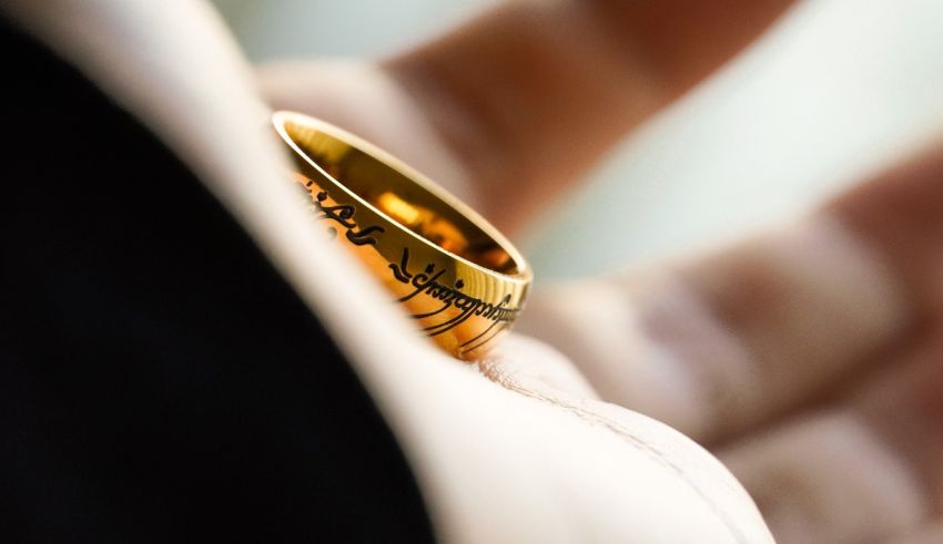 A person is holding a gold ring with the lord of the rings written on it.
