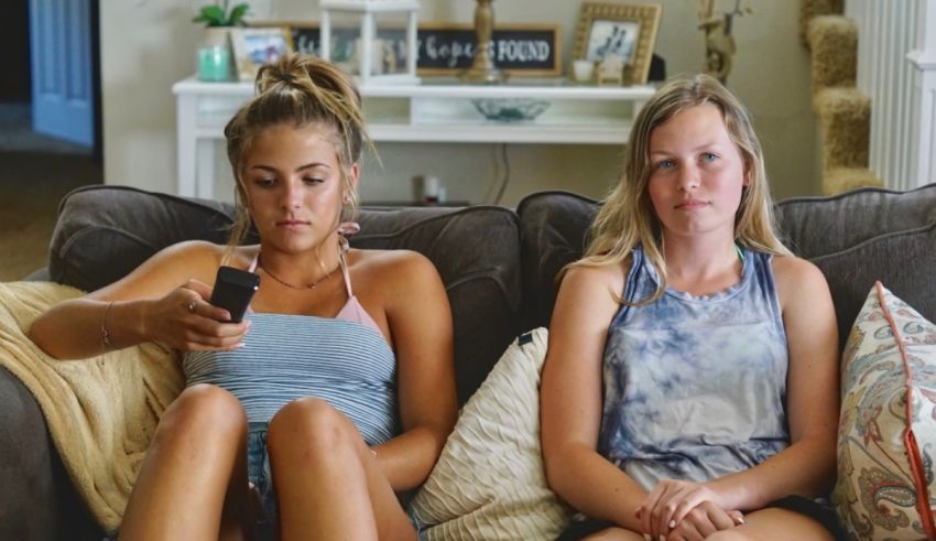 Two girls sitting on a couch looking at their phones.