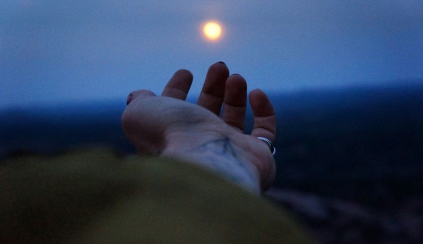 A person's hand reaching out to the moon.