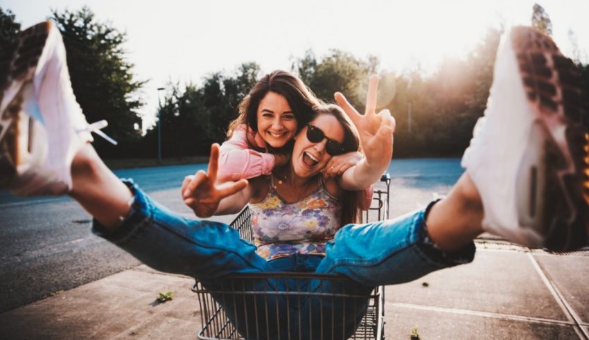 Two women sitting in a shopping cart and taking selfies.