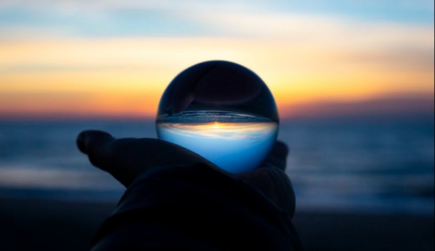 A person holding a glass ball in front of the ocean at sunset.