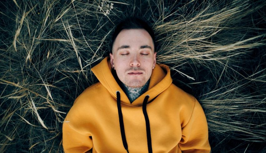 A man in a yellow hoodie laying in the grass.