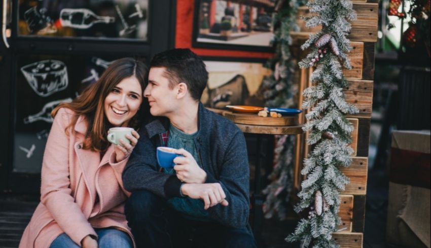 A couple is sitting on a bench with a cup of coffee in front of a christmas tree.