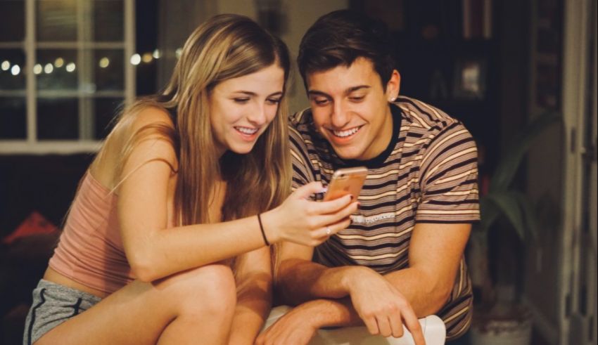 Two young people sitting on the floor looking at a cell phone.