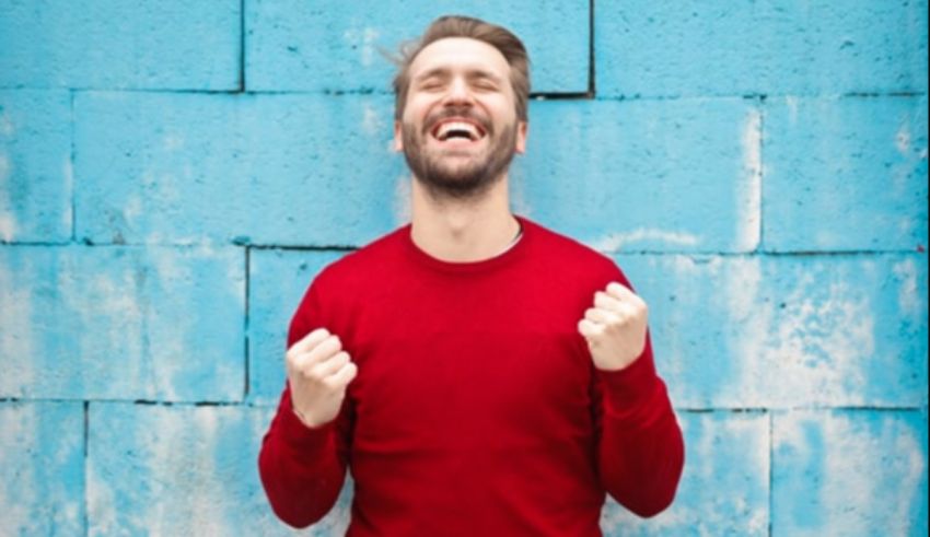 A man is laughing against a blue wall.