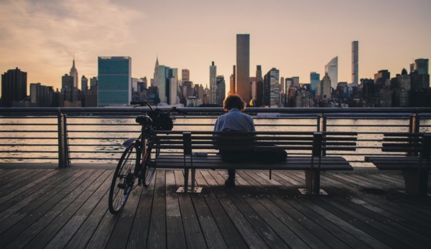 A woman sits on a bench overlooking the city at sunset.