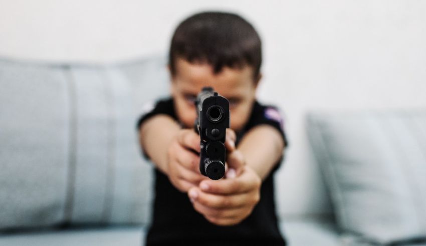 A young boy pointing a gun at a couch.
