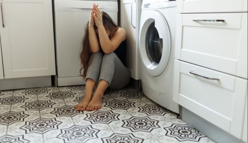 A woman sitting on the floor in front of a washing machine.