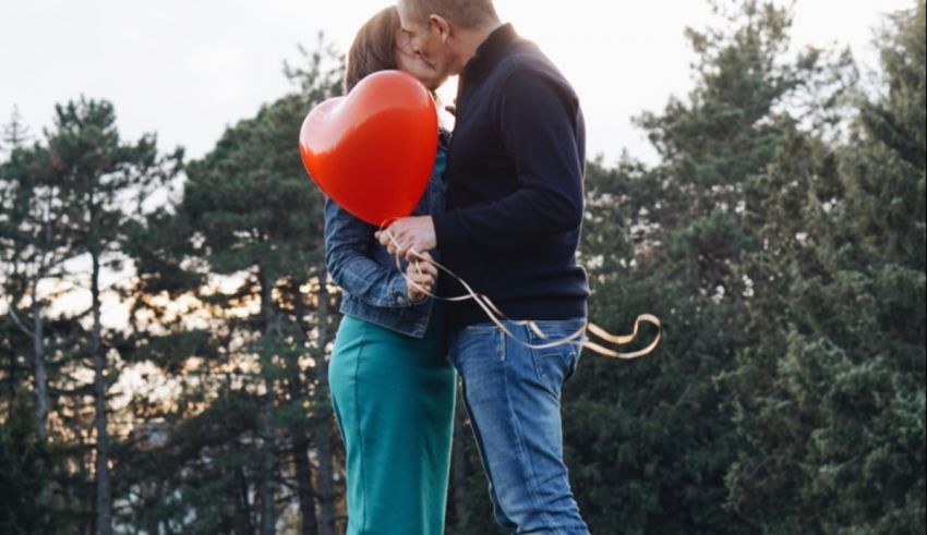 A couple kissing while holding a red heart balloon.