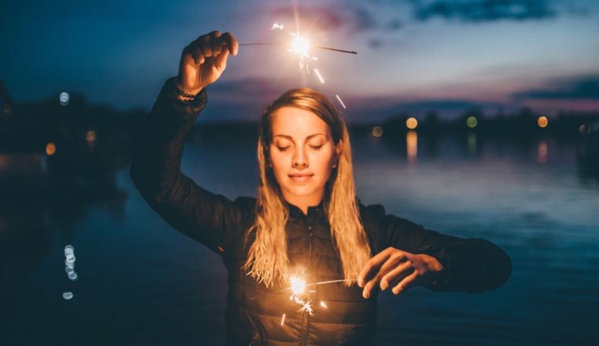 A woman holding a sparkler in front of a body of water.