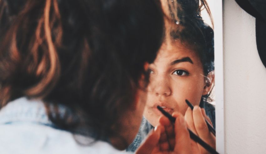 A woman applying makeup in front of a mirror.