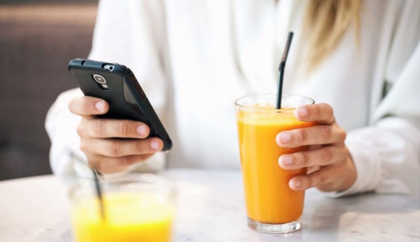 A woman holding a cell phone next to a glass of orange juice.