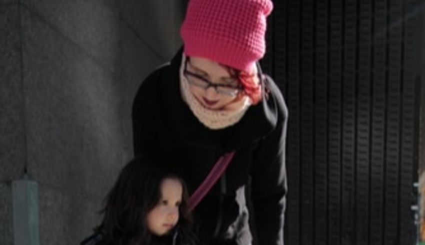 A woman in a pink hat is holding a little girl's hand.