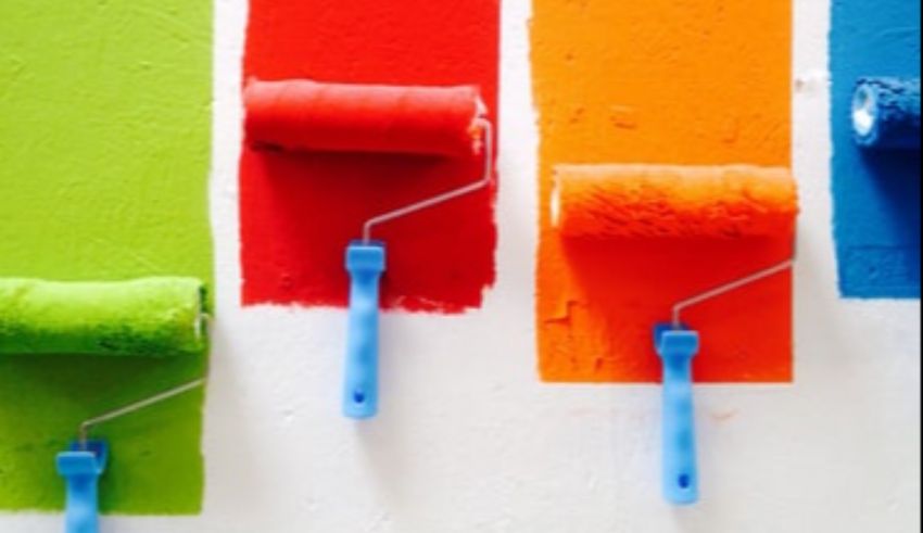 Paint rollers in different colors on a white wall.