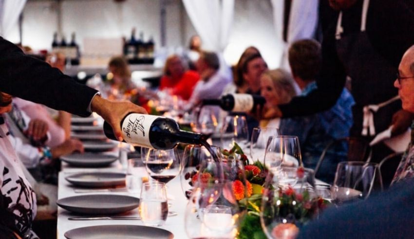 A man pouring wine at a long table full of people.