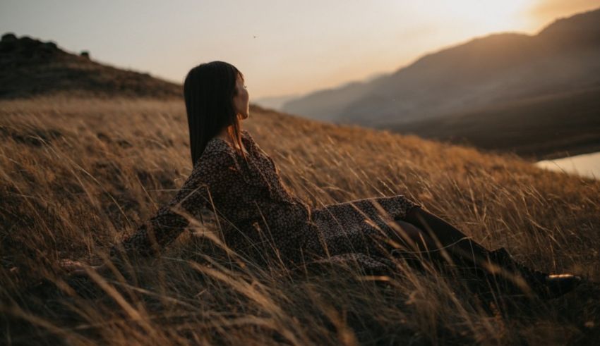 A woman sitting in tall grass at sunset.