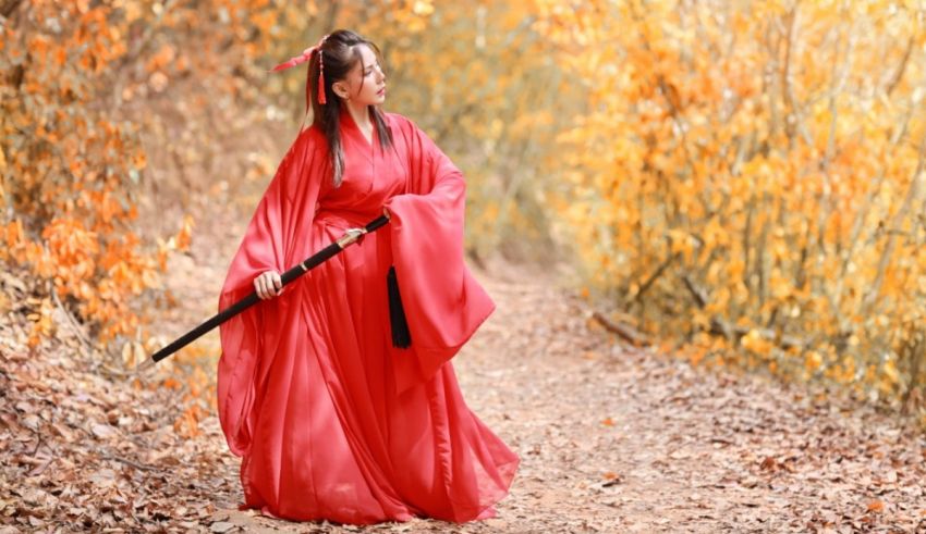 A woman in a red robe holding a sword in a wooded area.