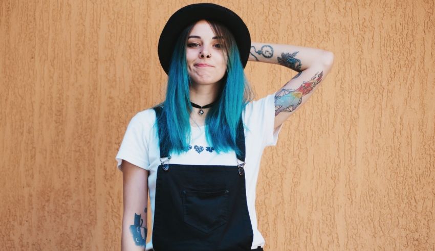 A young woman with blue hair wearing a hat and overalls.