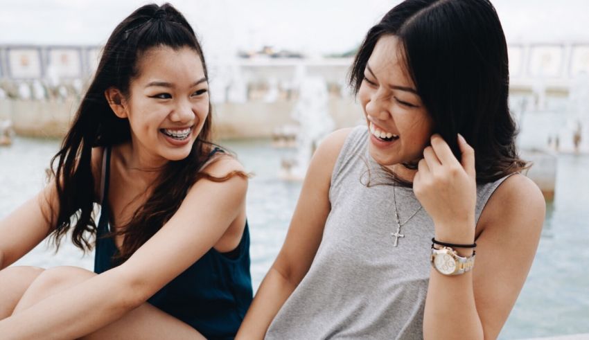 Two asian women laughing in front of a water fountain.