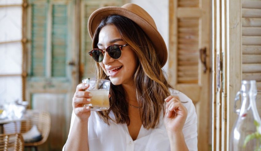 A woman wearing sunglasses and a hat is drinking a drink.