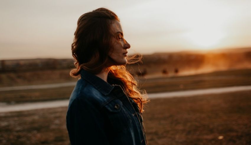 A woman in a denim jacket standing in a field at sunset.