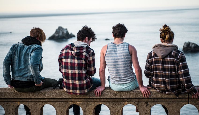 Four young men sitting on a ledge looking at the ocean.