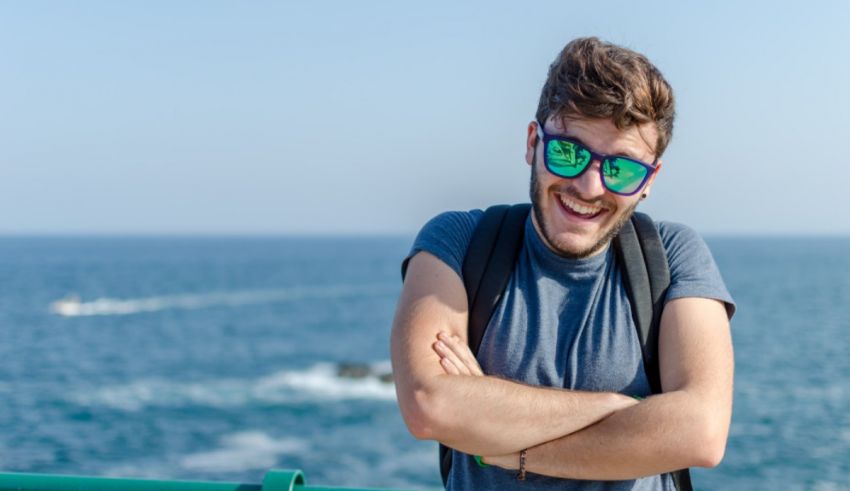 A young man wearing sunglasses is standing on a railing near the ocean.