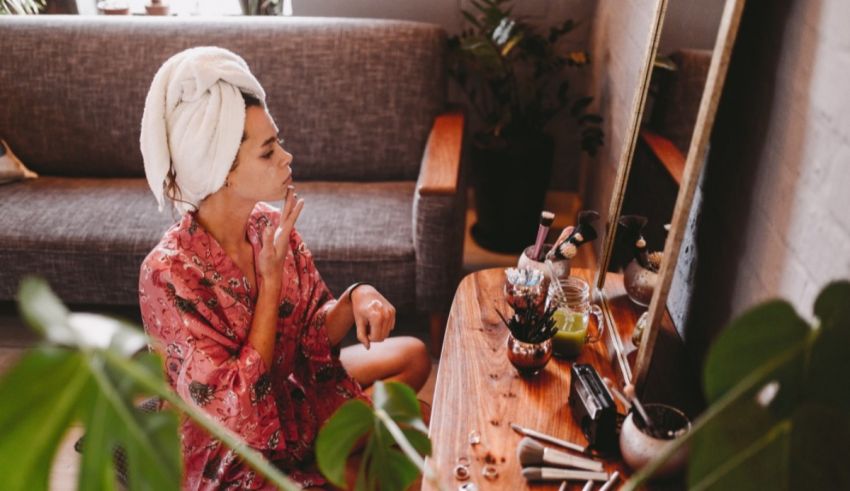 A woman in a robe is brushing her teeth in front of a plant.