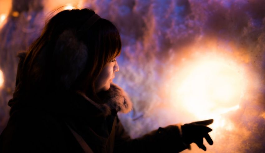 A girl is holding a candle in front of a snow wall.