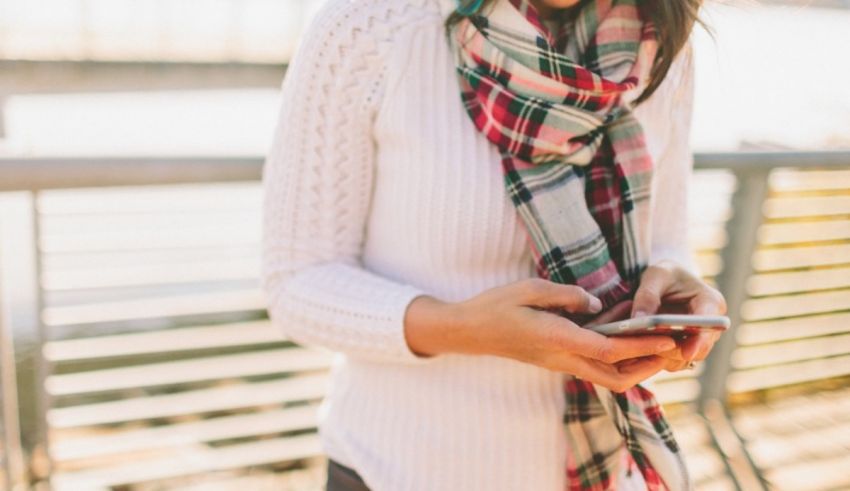 A woman wearing a plaid scarf and white sweater looking at her phone.