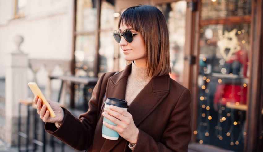 A woman is holding a cup of coffee and looking at her phone.