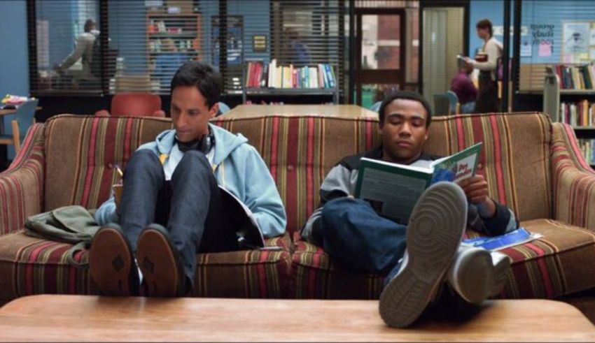 Two young men sitting on a couch in a library.