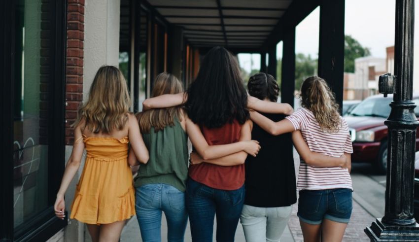 A group of girls standing on a sidewalk with their arms around each other.