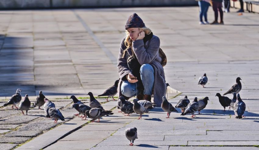 A woman feeding pigeons on the sidewalk.