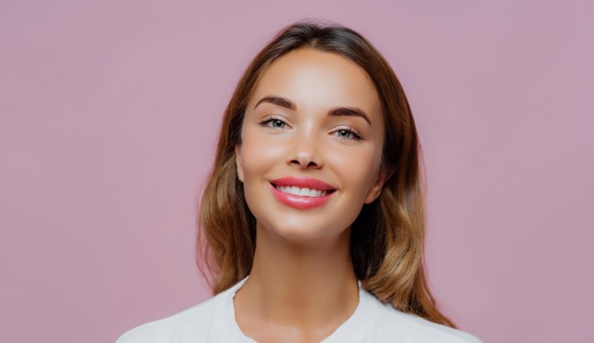 A young woman smiling against a pink background.