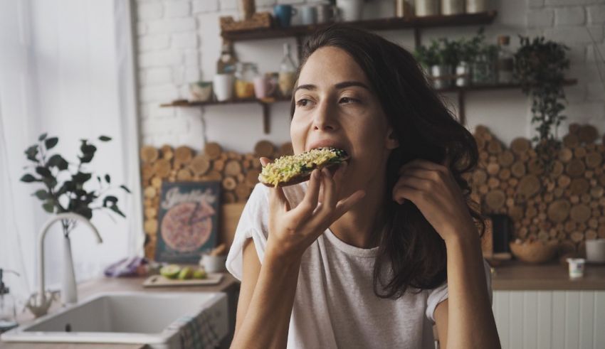 A woman is eating a piece of food in the kitchen.
