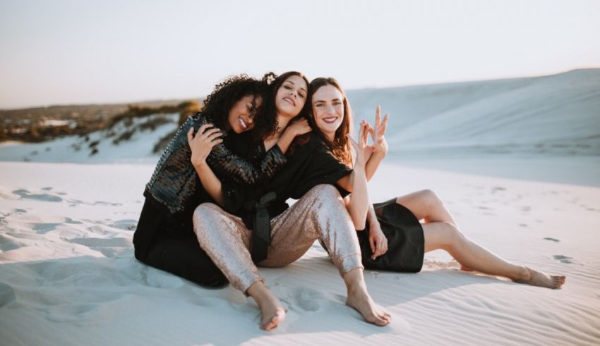 Three women sitting on a sand dune at sunset.