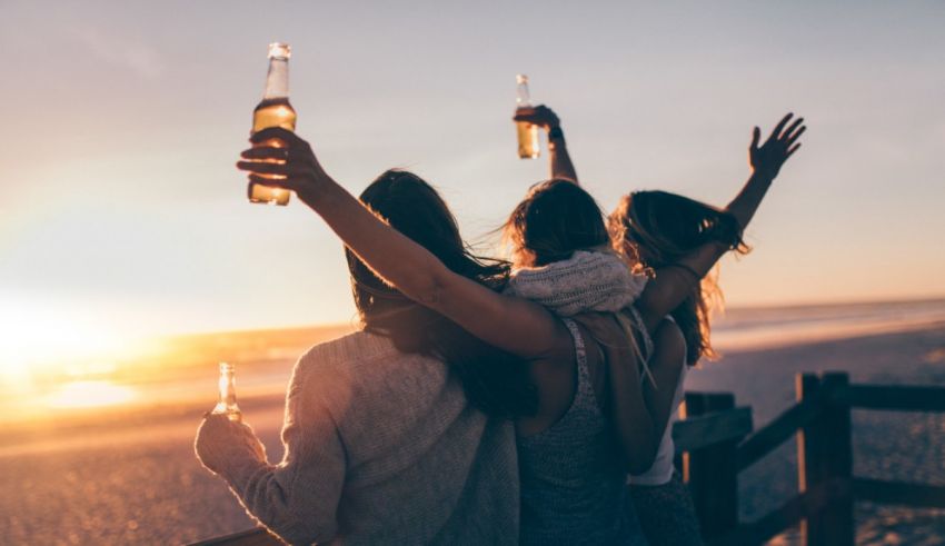 Three friends holding beer bottles on the beach at sunset.