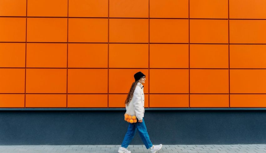 A woman walking in front of an orange wall.